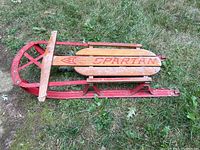Side angle photo showing the full length of the wooden and metal sled, highlighting the red painted metal frame and natural wooden slats with Spartan logo.