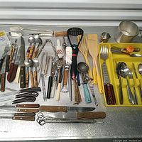Wide top-down view of a large assortment of vintage kitchen utensils including forks, knives, spatulas, tongs, ladles, and other miscellaneous items in mixed materials and colors.