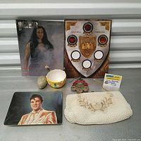 Overview of lot with Highlander catalog, shield plaque, ceramic cup, Christmas ornament, Elvis plate, and white beaded handbag
