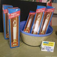 Lot of 6 battery candle lamps in their original boxes placed inside a blue basket theme bowl. Boxes are approximately 9 inches tall.