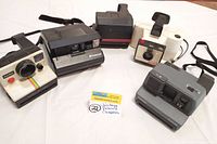 Group shot of all five vintage Polaroid instant cameras with seller's lot tag in front