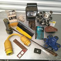 Overview of lot showing marine electric cord plug, screwdriver bits, sanding sponge, flashlight, scraper, string, 3 wheel movers dollies, small brush and metal piece