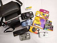 Photo showing entire lot of cameras including Polaroid Sun 600 LMS, Pentax Zoom 90, additional cameras and Kodak single-use cameras in packaging.