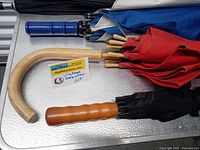 Five vintage umbrellas with varied handle styles and colors laid on a table, showing curved wooden handles and plastic/wood straight handles.