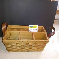 Front view of rectangular woven wood basket with leather handles and internal wooden compartments, placed on a white surface against black background.