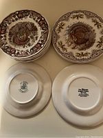 Stack of dessert plates featuring turkey design with fruit border, showing top decorative side and backstamp logos on plates
