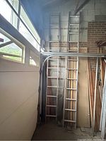 Photo showing two aluminum extension ladders with twelve rungs each leaning against a wall inside a garage.