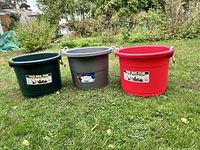 Photo showing three large plastic tubs on grass, green, gray, and red, each with handles and labels