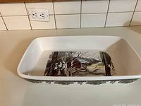Top-down view inside the rectangular ceramic baking dish showing the printed countryside barn and trees scene.