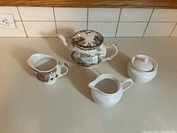 Front view of Friendly Village teapot, two creamers, and sugar bowl on countertop.