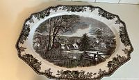 Top view of large ceramic serving platter with scenic village and floral border in brown tones.