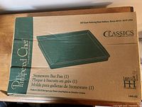 Photo of the Pampered Chef stoneware bar pan in its original box showing the product illustration and brand details.