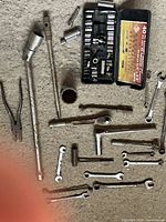 Photo showing assorted ratchets, sockets in case, extension bars, and wrenches laid on carpeted floor.