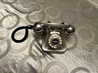 Full view of metal reproduction antique rotary dial phone showing its handset, coiled black cord, and rotary dial.