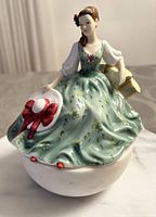 Front view of the Royal Doulton porcelain figurine showing the seated woman in green dress holding a white hat with red bow.