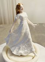 Porcelain figurine wearing white dress holding skirt, showing floral detail and light brown hair