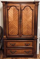 Front view of the solid wood wardrobe showing the two doors with decorative panels and two large drawers below with metal handles.