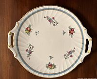 Top view of the round Spode pastry plate showing decorative floral and fruit patterns with blue and gold trim around the edge and two handles.