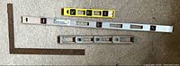 Photo shows four measuring and leveling tools on a grey surface: a large framing square, a wooden level, a long metal level, and a smaller metal level.