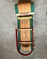 Top view of the children's wooden sled showing natural wood slats with green painted sections, red metal handlebar, and torpedo branding.
