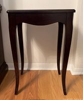 Front view of the small dark wooden side table showing curved legs and smooth top surface.