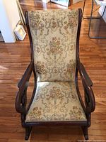 Front view showing floral tapestry fabric and wooden swan neck arms of the rocking chair.