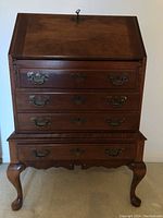 Front view of the antique Maddox secretary desk showing the slant top and three drawers with brass bail handles and keyholes.