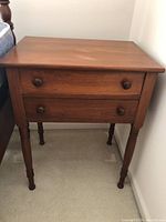Front view of one of the antique side tables showing two drawers with round wooden knobs and turned legs.