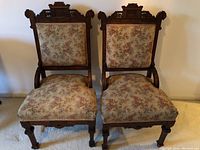 Pair of antique Victorian Eastlake style hip rest parlor chairs photographed side by side, showing full front view including wood carving and floral upholstery.