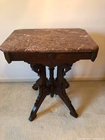 Overall view of marble top foyer table showing brown marble top with white veins and dark wooden base with intricate Victorian detailing.