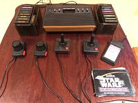 Top view photo showing the Atari CX-2600 console with two columns of game cartridges on each side and four controllers in front. Also shows the Star Wars game manual.