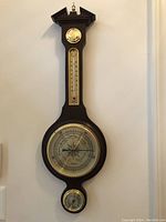 Full view of vintage wall barometer showing wooden casing, thermometer at top, large barometer dial in middle, and hygrometer at bottom, all with brass trim.