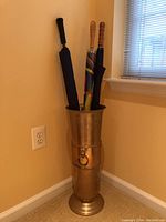 Full view of brass umbrella stand holding three umbrellas in a corner