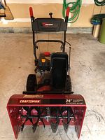 Front view of the entire snowblower showing housing, handles and wheels