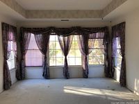 View of a large window with multiple sheer curtains in a purple and maroon floral pattern covering the panes, with rod pocket headers and gathered draping tied back.