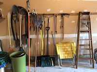 Wide view of garden tools hanging on wall, two yellow lawn chairs folded, and wooden stepladder
