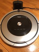Top view of iRobot Roomba robotic vacuum cleaner showing silver and black body, main CLEAN button, and additional control buttons.