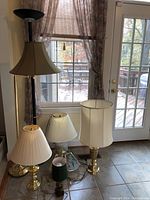 Four lamps grouped together near window, showing variety in size and style including standing and table lamps with different shades and bases
