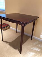 Angle view showing the rosewood tabletop with gently curved edges and polished finish along with one folding leg extended.