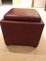 Side angle view of the brown leather-like storage hassock showing the cube shape and padded top.
