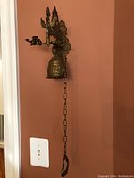 Side view of the brass wall-mounted bell showing the long chain and decorative bracket