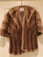 Full frontal image of the mink stole hung on a hanger showing collar, sleeves, and body of coat in light brown shade with label visible.