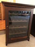 Front view of the wooden wine cabinet with a glass door showing four shelves with angled sections for storing wine bottles horizontally.