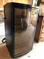 Full view of Haier wine cooler with glass door, showing metal wine racks inside and power cord on top.