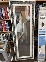 Two custom ceramic border mirrors, rectangular shape, reflecting a room with bookshelves, showing clear glass and white ceramic frames.