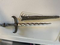 Photo of decorative Cleopatra dagger with wavy blade, detailed hilt, and ornate scabbard with engravings.