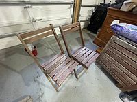 Two wooden folding chairs placed side by side showing the slatted wood design and foldable frames.