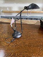 Black adjustable desk lamp on wooden surface with power cord visible