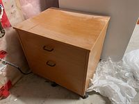 Photo of the Ikea 2 drawer wooden cabinet showing top and side with wheels, light brown finish, and black handles