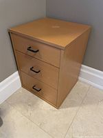 Front and right side view of the Ikea 3 drawer cabinet showing the light wood finish, black handles, and caster wheels on bottom.